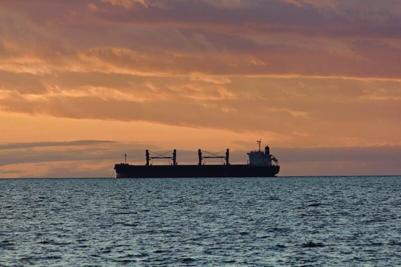 A silhouette of a ship underway in the distance at dusk