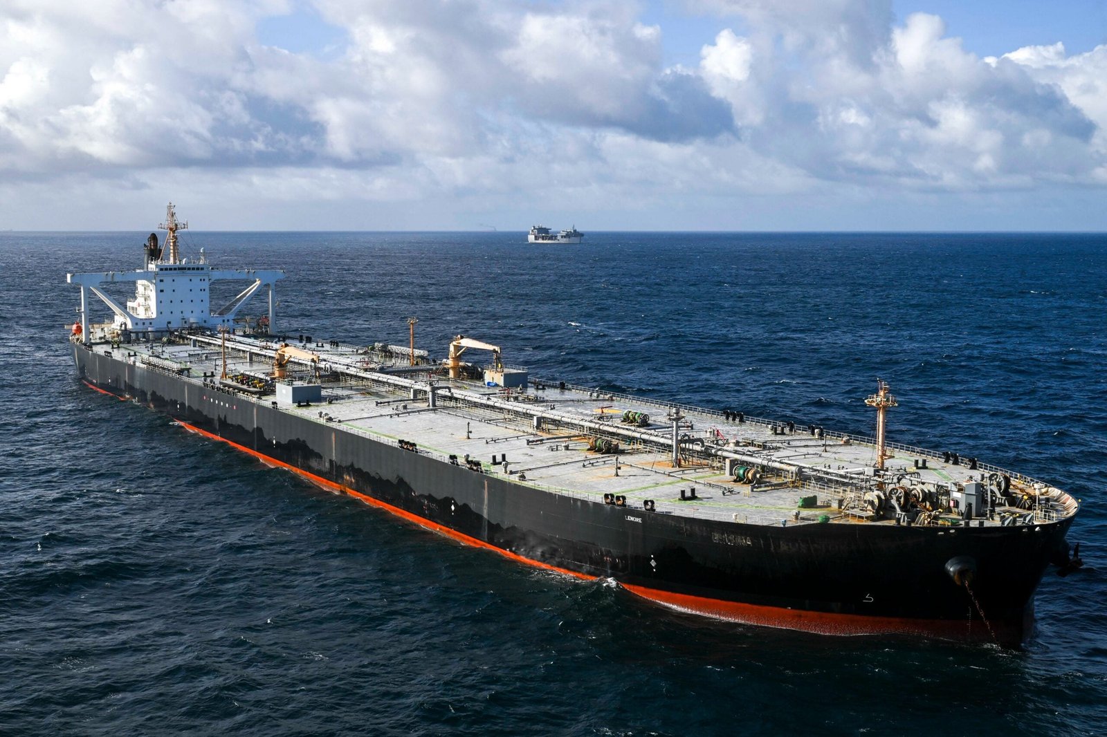 A large crude oil tanker identified as MT Davina sails in open ocean under partly cloudy skies. The black-hulled vessel is viewed from above and ahead, with another ship visible on the horizon in the background.
