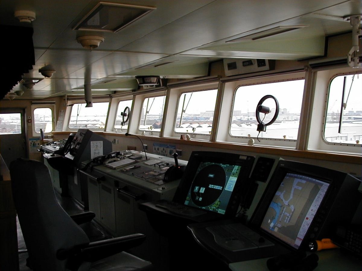 Ship navigation bridge with ECDIS chart and radar displays overlooking a port