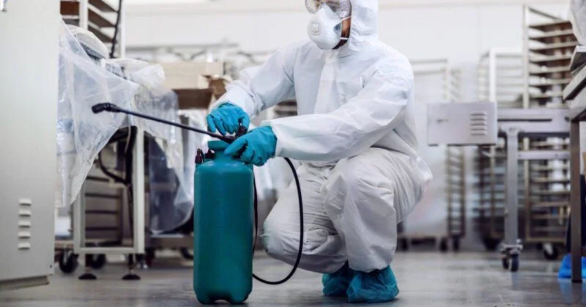 Worker in full protective suit and mask carrying out fumigation